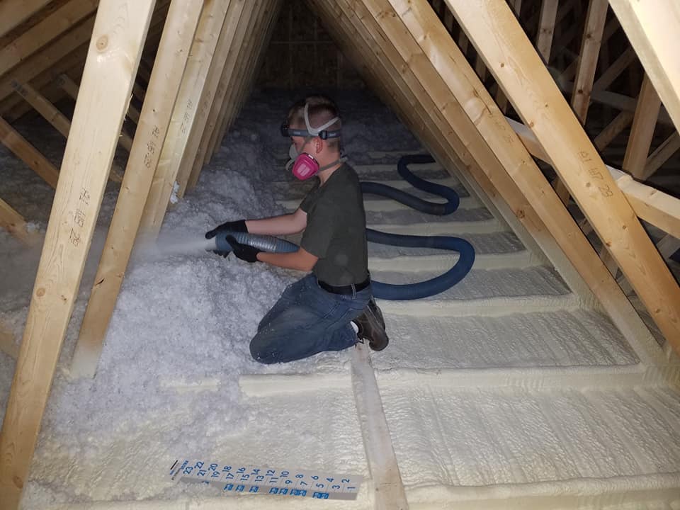 worker blowing insulation on top of spray foam insulation in an attic