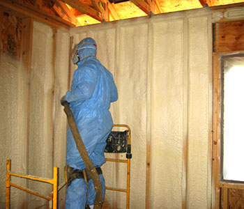 worker spaying foam insulation into wall cavities